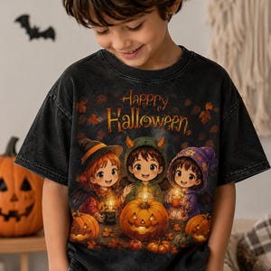 Op de afbeelding: Een zwart acid-wash T-shirt met een grafische print van drie kinderen in Halloween-kostuums die kaarsen vasthouden, omringd door pompoenen en herfstbladeren. De tekst "Happy Halloween" staat in het oranje boven de afgebeelde figuren.