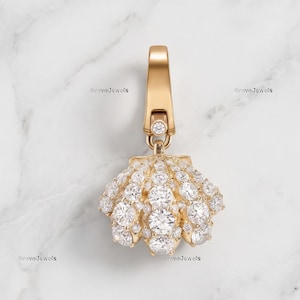 May include: A gold charm in the shape of a seashell, featuring a hinged bail at the top. The entire surface of the shell is encrusted with numerous small, round, clear, sparkling stones that catch the light, creating a textured, brilliant appearance.