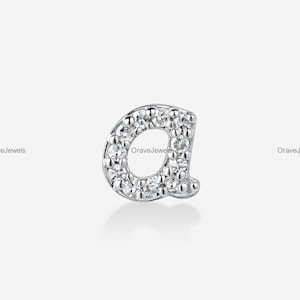 May include: A silver-toned letter a charm featuring a pavé-set surface with multiple small clear stones. The lowercase letter is crafted in a rounded font style and includes the text OraveJewels printed faintly in the background area.
