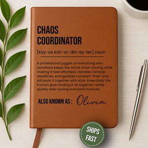 May include: A brown leather-bound notebook with the words "CHAOS COORDINATOR" in bold black letters. The definition of the term is printed below, along with the name "Olivia." A silver pen and a cup of coffee are on the right.