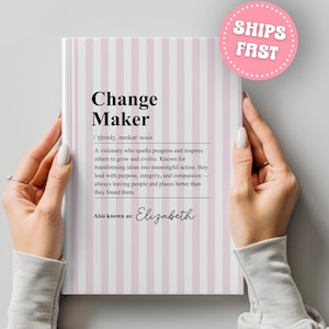 May include: A hardcover notebook with a pink and white striped cover. The title "Change Maker" is displayed in black, along with a definition. The notebook is also labeled "Also known as: Elizabeth".