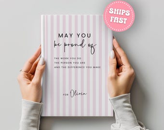 Puede incluir: Un cuaderno con una cubierta a rayas rosas y blancas. La cubierta presenta el texto "MAY YOU be proud of THE WORK YOU DO THE PERSON YOU ARE AND THE DIFFERENCE YOU MAKE FOR Olivia."