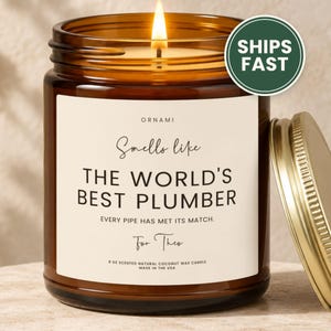 May include: A 9 oz scented natural coconut wax candle in an amber glass jar with a gold lid. The label reads: ORNAMI, Smells like THE WORLD'S BEST PLUMBER, EVERY PIPE HAS MET ITS MATCH, For Theo, 9 OZ SCENTED NATURAL COCONUT WAX CANDLE MADE IN THE USA.
