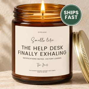 May include: A 9 oz scented natural coconut wax candle in an amber glass jar with a gold lid. The label reads: ORNAMI, Smells like THE HELP DESK FINALLY EXHALING, NOTIFICATIONS MUTED. VICTORY LOGGED., For Jack, 9 OZ SCENTED NATURAL COCONUT WAX CANDLE, MADE IN THE USA.