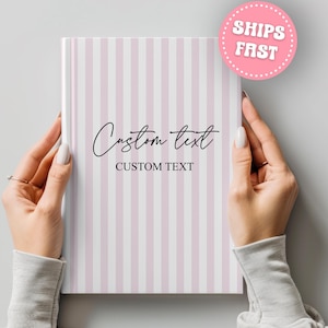 May include: A notebook with a pink and white striped cover. The cover features the words "Custom text" in a script font. A pink circle with the words "Ships Fast" is in the upper right corner.