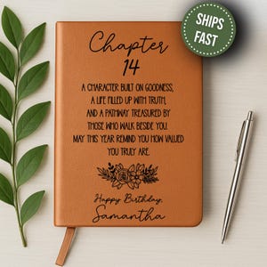 May include: A brown leather journal with the text "Chapter 14" and a birthday message. A silver pen rests beside the journal. The journal includes a ribbon bookmark and a floral design. A green circle with the words "SHIPS FAST" is in the upper right corner.