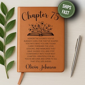 May include: A brown leather journal with the words "Chapter 75" and a floral design. The journal includes inspirational text and the name "Olivia Johnson". A silver pen rests beside the journal. A green circle with the words "Ships Fast" is in the upper right corner.