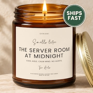 May include: A 9 oz scented natural coconut wax candle in an amber glass jar with a gold lid. The white label reads: ORNAMI, Smells like THE SERVER ROOM AT MIDNIGHT, COOL AISLE. CALM MIND. NO ALERTS., For Arlo, 9 OZ SCENTED NATURAL COCONUT WAX CANDLE.