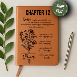 May include: A brown leather journal with the text "CHAPTER 12" and a floral design. The journal includes the name "Olivia" and inspirational text. A silver pen rests on the right side. A green circle with the words "SHIPS FAST" is in the upper right corner.