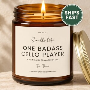 May include: A 9 oz scented natural coconut wax candle in an amber glass jar with a gold lid. The label reads: ORNAMI, Smells like ONE BADASS CELLO PLAYER, BOW IN HAND. BRAVADO ON CUE. For Finn, 9 OZ SCENTED NATURAL COCONUT WAX CANDLE MADE IN THE USA.