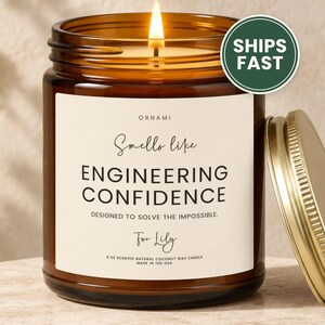 May include: A 9 oz scented natural coconut wax candle in an amber glass jar with a gold lid. The label reads ORNAMI, Smells like ENGINEERING CONFIDENCE, DESIGNED TO SOLVE THE IMPOSSIBLE, For Lily, 9 OZ SCENTED NATURAL COCONUT WAX CANDLE MADE IN THE USA.