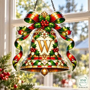 May include: A stained glass style hanging ornament shaped like a bell with a large letter W in the centre. The design features red ribbons, green holly leaves, red berries, and white flowers. It is suspended by a black chain against a window.