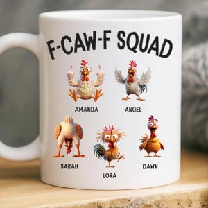 May include: White ceramic mug featuring the text "F-CAW-F SQUAD" in black. The mug displays cartoon chickens with various expressions, each labeled with a name: Amanda, Angel, Sarah, Lora, and Dawn. The mug has a white handle.