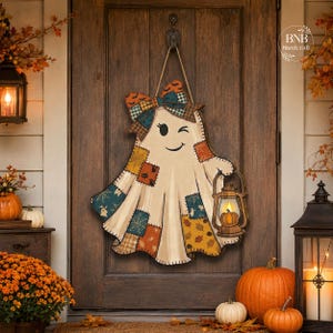 May include: A wooden ghost-shaped door hanger featuring a patchwork design with orange, teal, and brown patterns, a large bow at the top, and a hand holding a lantern with a pumpkin graphic. The ghost has a winking face and hangs by a rope.