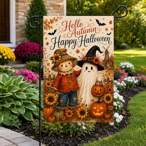 Op de afbeelding: Een decoratieve tuin vlag met een vogelverschrikker en een geest met een heksenhoed, omringd door zonnebloemen en pompoenen. De tekst luidt Hello Autumn Happy Halloween. Het ontwerp bevat vleermuizen, herfstbladeren en een windmolen.