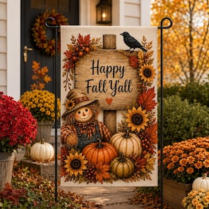 May include: A rectangular garden flag featuring a wooden sign with the text Happy Fall Y'all, a scarecrow, pumpkins, sunflowers, autumn leaves, and a black crow. The flag is displayed on a black metal stand in an outdoor setting.