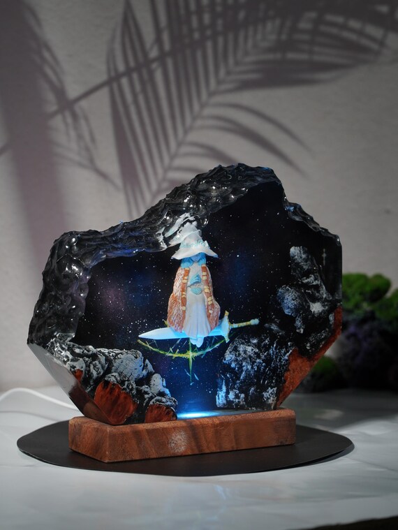 A hand-cast resin diorama lamp where a moon witch scene glows in cosmic blue — it's a miniature fantasy world you plug in, not just a light.