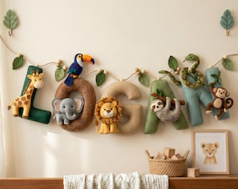 May include: A decorative felt garland spelling the name LOGAN, featuring plush animal figures including a giraffe, toucan, elephant, lion, sloth, snake, and monkey attached to individual fabric letters, accented with small wooden beads and felt leaves.