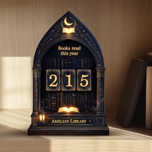 May include: A dark blue wooden bookshelf-shaped display with the text "Books read this year" and the number "215" in gold. The display also features a crescent moon and an open book at the top, and the text "AMELIA'S LIBRARY" at the bottom.