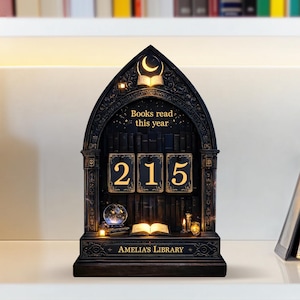 May include: A black wooden bookshelf-shaped display with the text "Books read this year" and the number "215". The display has a moon and book design at the top and the words "AMELIA'S LIBRARY" at the bottom. It includes small lights and a crystal ball.