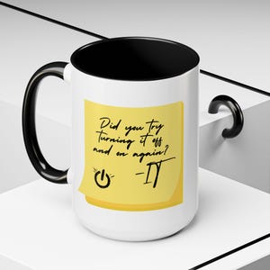 May include: White ceramic mug with a black interior, handle, and rim. A yellow sticky note is adhered to the mug, with the text "Did you try turning it off and on again?" and a power symbol.