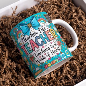 May include: A white ceramic mug featuring a vibrant turquoise background with a large blue glittery bow and colorful school-themed illustrations. The text reads Teacher Life, TEACHER, Teaching is a Work of Heart, and LEARN on blocks.