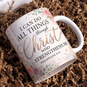 May include: White ceramic mug with a curved handle, decorated with floral designs in pink, purple, and green. The mug features the text "I CAN DO ALL THINGS through Christ who strengthens me Philippians 4:13."