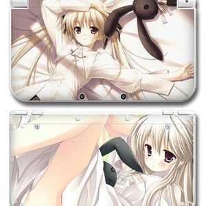 Może przedstawiać: Biała skórka do konsoli Nintendo 3DS z grafiką w stylu anime. Przedstawia blondwłosą postać w białym stroju z czarną pluszową zabawką królika. Skórka pokrywa górną i dolną część konsoli.