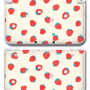 Puede incluir: Una funda crema para Nintendo 3DS con un patrón repetido de fresas rojas con tallos verdes. Algunas fresas tienen caras de dibujos animados o pequeños personajes de animales. La funda tiene bordes y botones blancos.