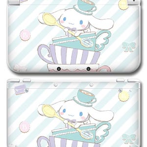 May include: White Nintendo 3DS case with a cartoon character wearing a teacup hat and holding a spoon, sitting on stacked teacups. The design has a light blue and white striped background, with bows and the number 15.