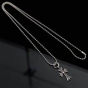 May include: Silver necklace with a cross pendant. The pendant has an intricate design with a central detail. The chain is made of small, round beads. The background is a dark, reflective surface. The necklace is a stylish accessory.