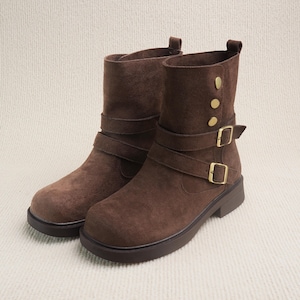 May include: A pair of brown suede ankle boots. The boots have a rounded toe, a low heel, and a strap with a buckle around the ankle. Additional straps and gold-colored buttons adorn the upper shaft. The boots are designed for everyday wear.