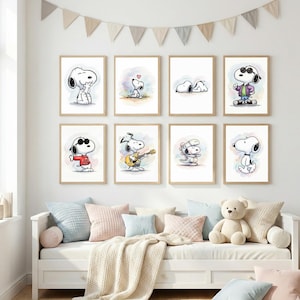 May include: A collection of eight framed Snoopy art prints. Each print features a different watercolor illustration of Snoopy in various poses, including playing guitar and wearing sunglasses. The prints are displayed above a white daybed with pastel-colored pillows and a teddy bear.