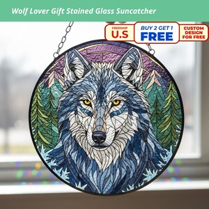 Könnte beinhalten: Runder Glas-Suncatcher mit Wolfsmotiv. Der Wolf ist in Blau- und Grautönen gehalten, mit gelben Augen. Der Hintergrund zeigt Berge und Bäume. Der Suncatcher wird an einer Kette aufgehängt und ist ein dekoratives Element.