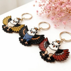 May include: Three leather eagle keychains with gold-colored key rings. The eagles have outstretched wings and are colored yellow, blue, and red. Each keychain has a white head and a black body.
