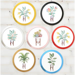 May include: A collection of seven round wall art pieces featuring watercolor illustrations of various plants in white pots with wooden stands. Each piece has a different colored border, including gold, black, white, pink, red, brown, and blue.