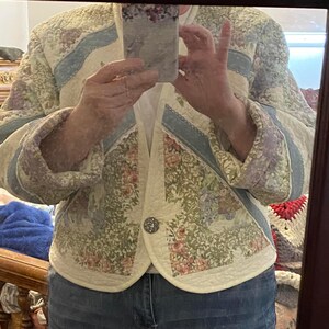May include: A white quilted jacket with a floral print and blue trim. The jacket has a button closure and is made of a soft, comfortable fabric.