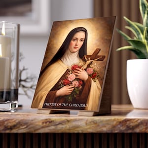 May include: A wooden plaque featuring a portrait of St. Therese of the Child Jesus, holding a crucifix and flowers. The image has a warm color palette with a golden halo. The text "ST. THERESE OF THE CHILD JESUS" is printed at the bottom.
