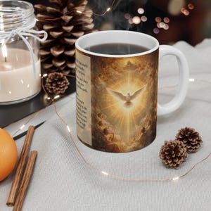 May include: White ceramic coffee mug with a religious image of a dove surrounded by clouds and light. The mug has a white handle and a dark liquid inside. Text is printed on the side of the mug.