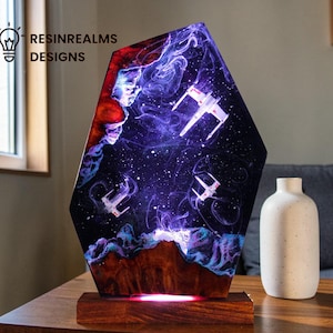 Könnte beinhalten: Dekorative Harzlampe mit einer Weltraumszene mit weißen Sternenjägern vor einem lila-blauen Nebel. Die Lampe hat einen Holzsockel mit rotem Leuchten und dem Text "RESINREALMS DESIGNS".