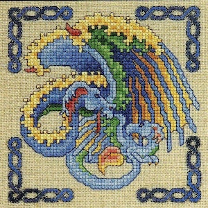 Könnte beinhalten: Eine Kreuzstichstickerei auf beigem Stoff mit einem zentralen Drachen mit blauen, grünen und gelben Schuppen. Der Drache ist von einem dunkelblauen, geknoteten Rand umgeben. Das Design verwendet ein gitterartiges Stichmuster für das Bild.
