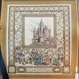 Könnte beinhalten: Ein gerahmtes Kreuzstich-Stickbild mit einer zentralen Burgdarstellung, umgeben von einem Alphabet-Rahmen von A bis Z. Unter der Burg sind fünf Figuren in historischer Kleidung abgebildet, mit den Ziffern 0 bis 9 am unteren Rand.
