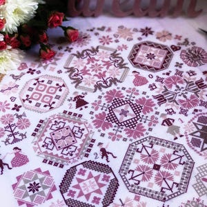 May include: White fabric with a cross-stitch design in shades of pink and gray. The design features geometric shapes, floral patterns, and small figures. The word "dream" is visible in the background, along with flowers.