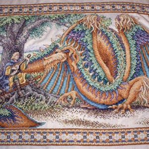 Könnte beinhalten: Eine detaillierte Kreuzstichstickerei, die eine Person zeigt, die unter einem großen Baum Laute spielt, neben einem großen, mehrfarbigen Drachen mit Flügeln. Die Szene ist von einer dekorativen, gemusterten Bordüre auf weißem Stoff umgeben.