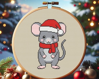 Op de afbeelding: Kruissteekborduurwerk in een houten hoepel met een grijze muis met een rode kerstmuts en sjaal. De muis is gecentreerd op een beige stoffen achtergrond. De borduursel is geplaatst tegen een feestelijke vakantieachtergrond.