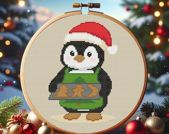 May include: A cross-stitch embroidery hoop featuring a cartoon penguin wearing a Santa hat and green apron, holding a tray of cookies. The penguin is black, white, and brown, with a red and white hat. The embroidery is set in a wooden hoop.