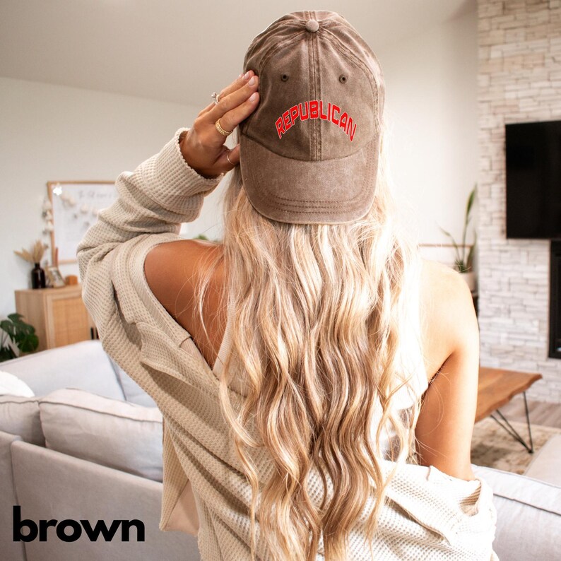 May include: A brown baseball cap with the word "REPUBLICAN" in red lettering. The cap is worn by a person with long blonde hair. The person is wearing a beige sweater.