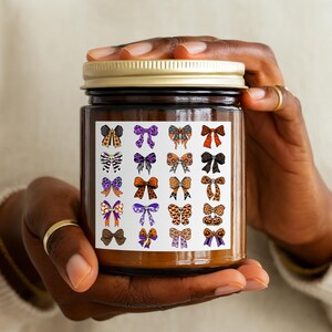 May include: A brown glass jar with a gold lid, held by a person. The jar has a white label with a grid of colorful bow illustrations. The bows feature various patterns and colors, including orange, purple, and leopard print, creating a festive and decorative design.