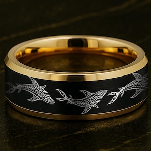 May include: A gold-toned ring with a black band featuring a repeating shark design in silver. The ring has a polished gold interior and a matte black exterior band. The sharks are stylized with intricate details.