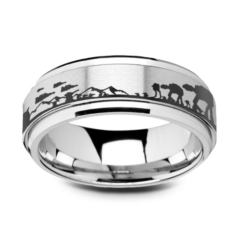 May include: A silver ring with a black etched design depicting a mountain range and AT-AT walker silhouettes. The ring has a polished finish and a beveled edge, with a sci-fi theme.